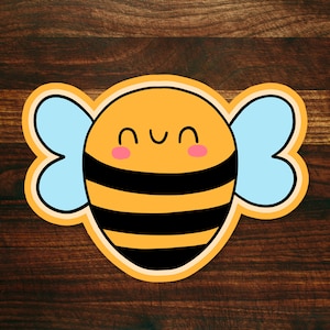 May include: A cartoon bee with black and yellow stripes, blue wings, and a smiling face. The bee is on a brown wooden background.
