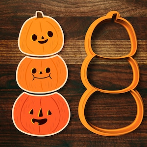 May include: A set of three orange pumpkin cookie cutters, stacked on top of each other. The top pumpkin has a simple jack-o'-lantern face, the middle pumpkin has a smiling mouth, and the bottom pumpkin has a more detailed jack-o'-lantern face.
