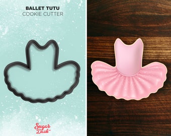 Op de afbeelding: Een zwarte plastic koekjesvormer in de vorm van een ballerina tutu. De vormer bevindt zich op een lichtblauwe achtergrond met witte stippen. De tekst "Ballet Tutu Cookie Cutter" bevindt zich boven de vormer. De tekst "Sugar Dash" bevindt zich onder de vormer.