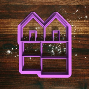 May include: Purple plastic cookie cutter shaped like a two-story house with windows and a door. The cutter is on a wooden surface.