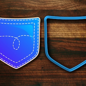 May include: A blue plastic cookie cutter in the shape of a pocket with a stitched outline. The cutter is on a brown wooden surface.