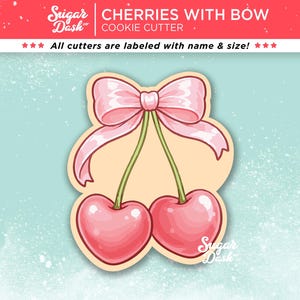 May include: A cookie cutter in the shape of two cherries with a pink bow. The cherries are a gradient of pink and red, with green stems. The text "CHERRIES WITH BOW COOKIE CUTTER" is at the top.