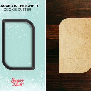 May include: A black cookie cutter in the shape of a rounded rectangle with a rounded top corner. The cookie cutter is on a light blue background with white speckles. The text "PLAQUE #13 THE SWIFTY COOKIE CUTTER" is above the cookie cutter. The text "Sugar Dash" is below the cookie cutter.