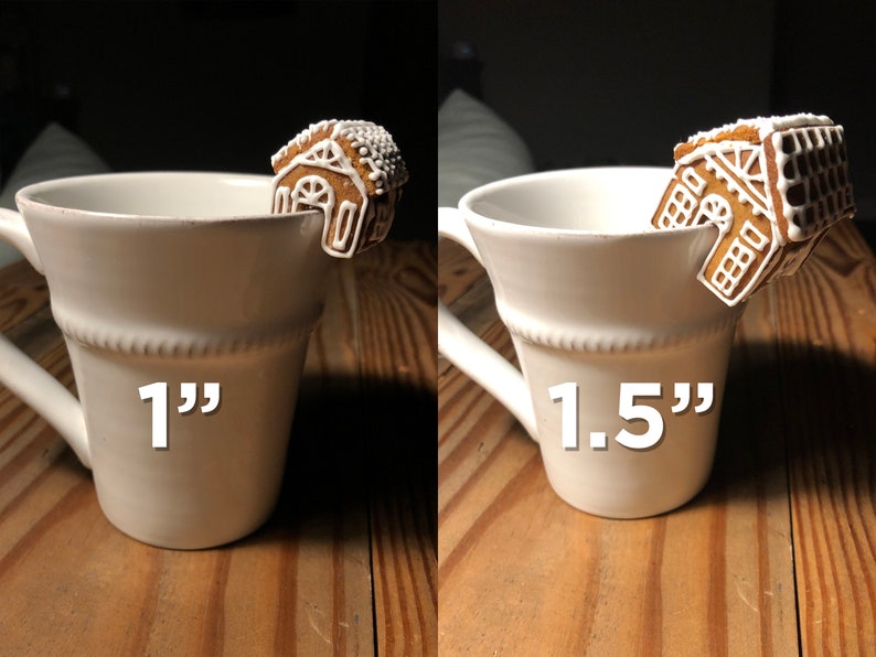 May include: Two white ceramic mugs with gingerbread house cookie stirrers. The mug on the left has a 1" gingerbread house stirrer and the mug on the right has a 1.5" gingerbread house stirrer.