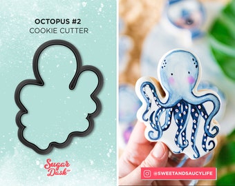 May include: A black cookie cutter shaped like an octopus. The cutter is on a light blue background with white speckles. The text "Octopus #2 Cookie Cutter" is above the cutter. The text "Sugar Dash" is below the cutter.