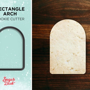 May include: A black metal cookie cutter in the shape of a rectangle arch. The cookie cutter is on a light blue background with white snowflakes. The text "Rectangle Arch Cookie Cutter" is above the cookie cutter. The text "Sugar Dash" is below the cookie cutter.
