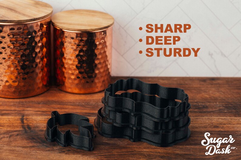 Puede incluir: Un juego de cuatro cortadores de galletas de pl&aacute;stico negro en forma de marco decorativo. Los cortadores est&aacute;n apilados uno encima del otro. El texto "SHARP", "DEEP" y "STURDY" est&aacute; escrito en naranja sobre fondo blanco. El texto "Sugar Dash co." est&aacute; escrito en blanco sobre fondo negro.