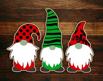 May include: Three wooden gnome cutouts with white beards, green noses, and red and black hats. One hat has black polka dots, another has green and black stripes, and the third has a black floral design.