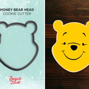 May include: A black cookie cutter shaped like Winnie the Pooh's head. The text "HONEY BEAR HEAD COOKIE CUTTER" is above the cutter. The text "Sugar Dash" is below the cutter.