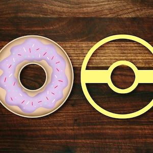 May include: A purple and white frosted donut with pink sprinkles on a brown wooden surface. Next to the donut is a yellow circle with a yellow band across the middle.