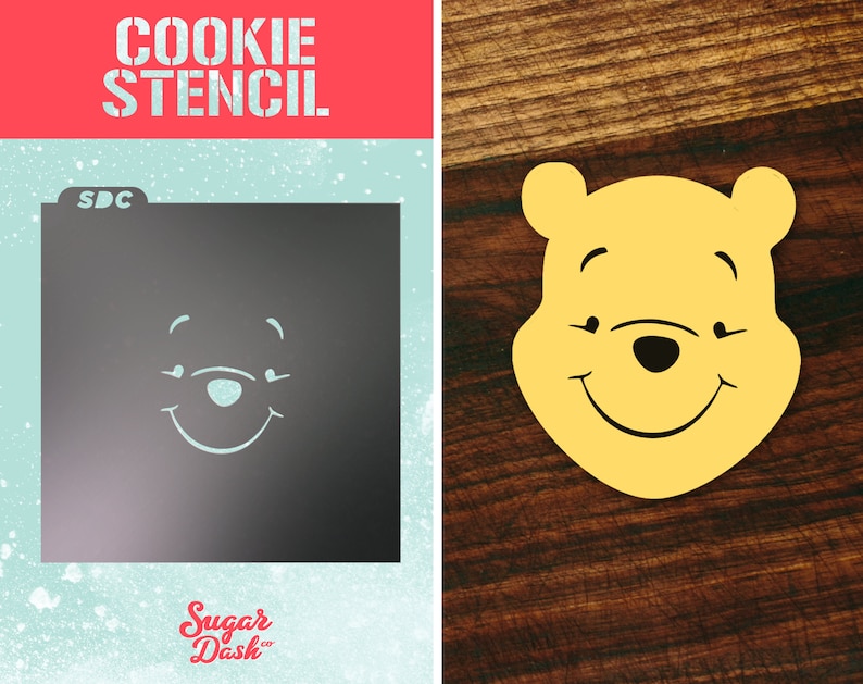 May include: A cookie stencil featuring a smiling Winnie the Pooh face. The stencil is made of plastic and is designed for use with cookie dough. The stencil is shown on a blue background with the words "Cookie Stencil" and "Sugar Dash" printed on it.