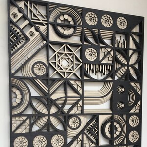 May include: A black and beige geometric wall art piece made of layered wood. The design features circles, squares, and triangles.
