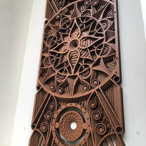 Puede incluir: Una pieza de arte de pared de madera con un dise&ntilde;o geom&eacute;trico intrincado. El dise&ntilde;o presenta un c&iacute;rculo central con un patr&oacute;n en espiral y est&aacute; rodeado de c&iacute;rculos y l&iacute;neas m&aacute;s peque&ntilde;os. La pieza est&aacute; hecha de m&uacute;ltiples capas de madera, creando un efecto 3D.