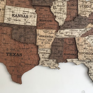 May include: A wooden map of the United States with each state outlined and labelled. The map is made of different shades of brown wood and has a distressed look. The state names are printed in black.