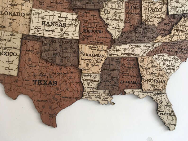 May include: A wooden map of the United States with each state outlined and labelled. The map is made of different shades of brown wood and has a distressed look. The state names are printed in black.
