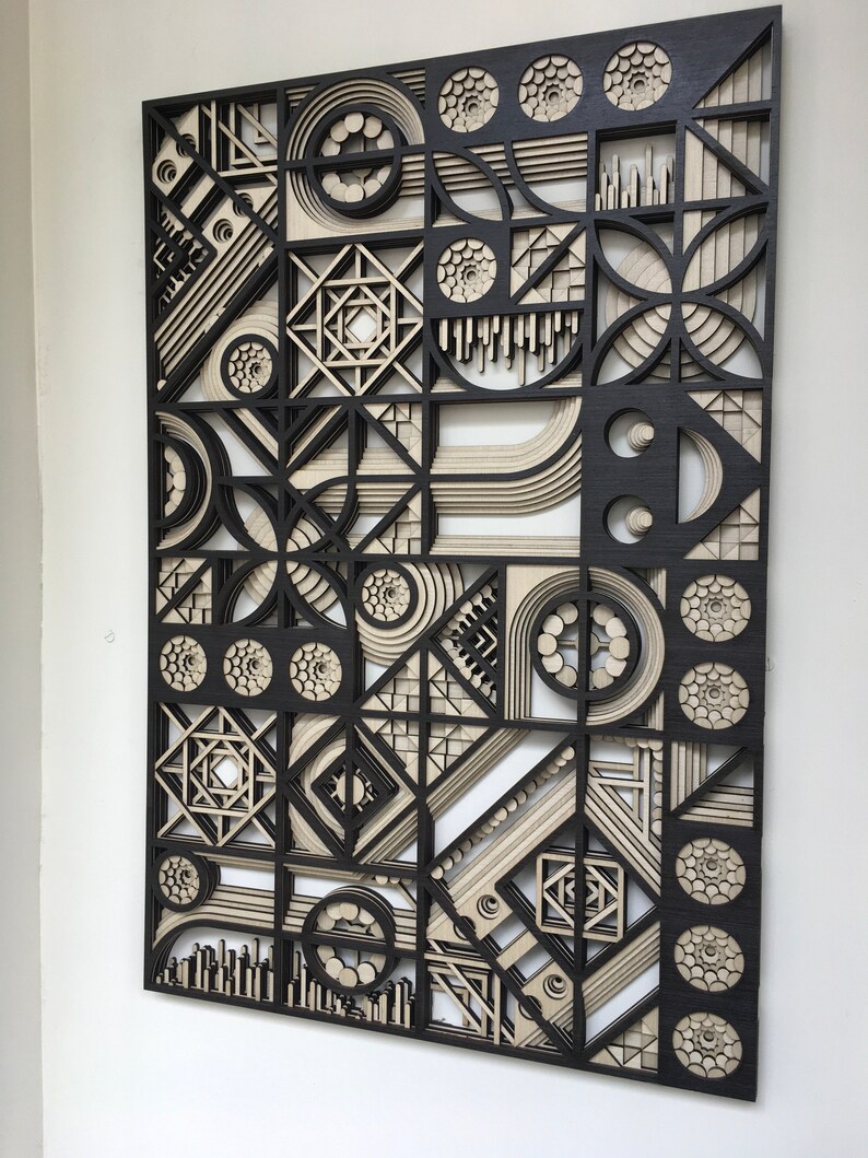 May include: A black and white geometric wall art piece made of layered wood. The design features circles, squares, and other shapes in a repeating pattern.