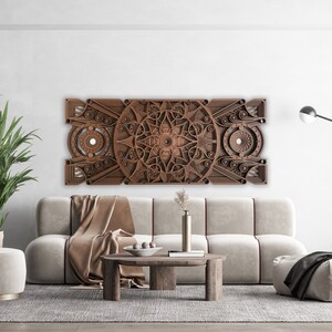 Puede incluir: Una pieza de arte de pared de madera marr&oacute;n con un dise&ntilde;o geom&eacute;trico. La pieza de arte est&aacute; colgada sobre un sof&aacute; blanco con una manta de tiro marr&oacute;n. Hay una mesa peque&ntilde;a delante del sof&aacute; con un jarr&oacute;n de flores encima.