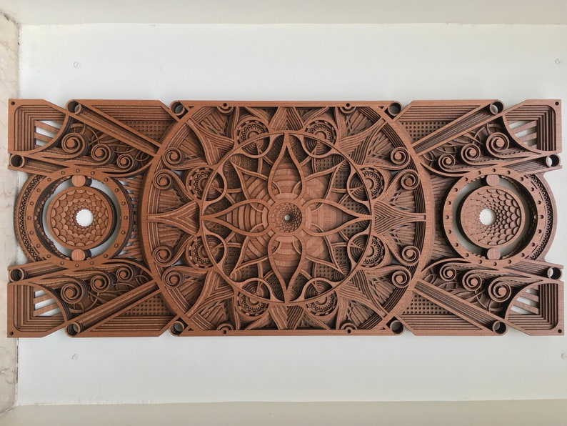Puede incluir: Una pieza de arte de pared de madera marr&oacute;n con un dise&ntilde;o geom&eacute;trico. El dise&ntilde;o presenta un c&iacute;rculo central con patrones intrincados y dos c&iacute;rculos m&aacute;s peque&ntilde;os a cada lado.