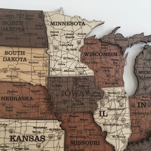May include: A wooden map of the Midwestern United States, with each state outlined in a different shade of brown. The states are labelled with their names and major cities. The map is a jigsaw puzzle, with each state a separate piece.