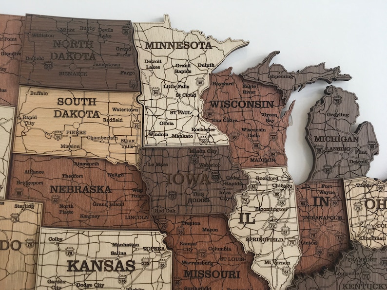 May include: A wooden map of the Midwestern United States, with each state outlined in a different shade of brown. The states are labelled with their names and major cities. The map is a jigsaw puzzle, with each state a separate piece.