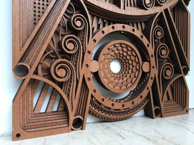 Puede incluir: Un primer plano de una pieza de arte de pared de madera con intrincados patrones geom&eacute;tricos y un dise&ntilde;o circular en el centro. La pieza est&aacute; hecha de m&uacute;ltiples capas de madera, creando un efecto 3D.