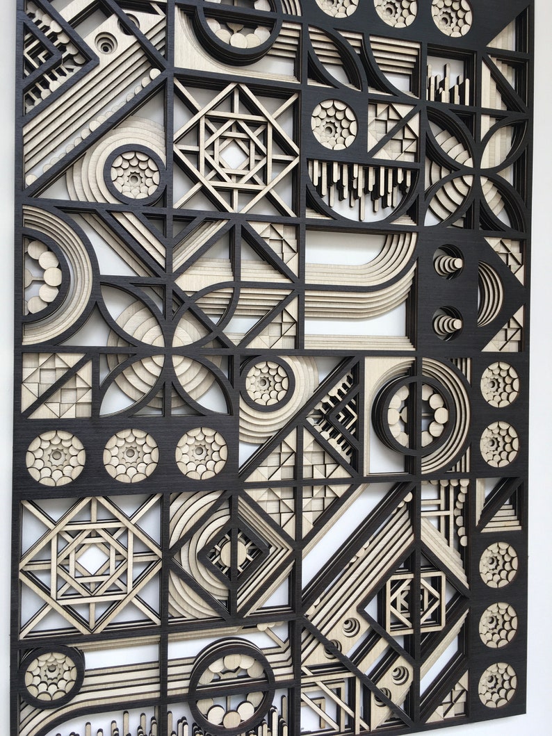 May include: A black and white geometric wall art piece made of wood. The piece features a variety of shapes, including circles, squares, and triangles. The shapes are layered on top of each other to create a three-dimensional effect.
