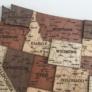 May include: A wooden jigsaw puzzle map of the United States, with each state individually cut out and labelled. The puzzle pieces are arranged in a way that shows the geographical location of each state. The puzzle is made of light brown wood and has a natural finish.