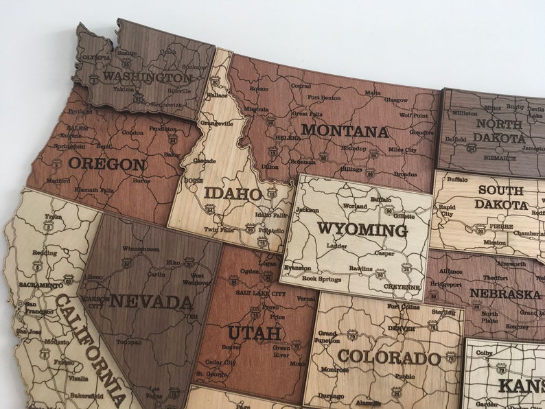 May include: A wooden jigsaw puzzle map of the United States, with each state individually cut out and labelled. The puzzle pieces are arranged in a way that shows the geographical location of each state. The puzzle is made of light brown wood and has a natural finish.
