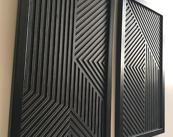 May include: Two black framed wall art pieces with a geometric pattern of overlapping lines creating a 3D effect.