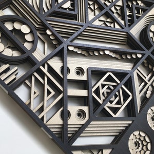 May include: A black and white geometric wall art piece made of layered wood. The design features circles, squares, and triangles in a complex pattern.