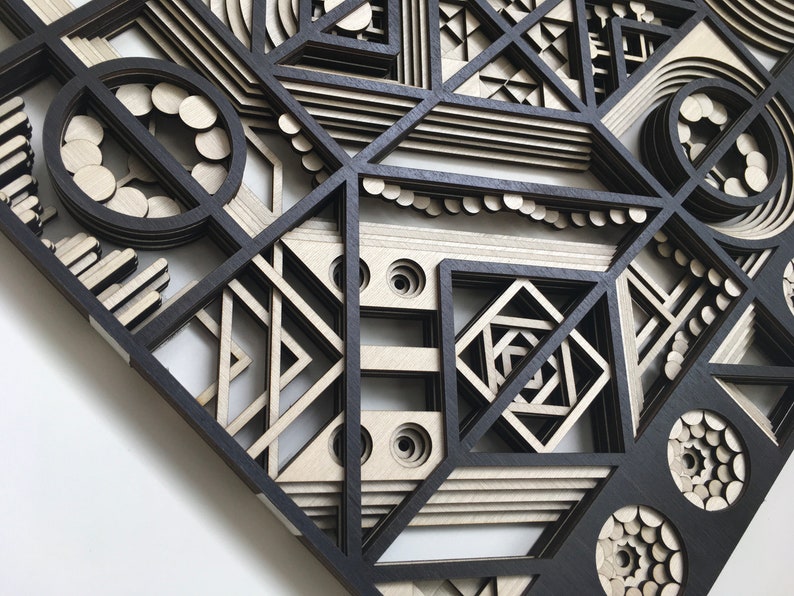 May include: A black and white geometric wall art piece made of layered wood. The design features circles, squares, and triangles in a complex pattern.
