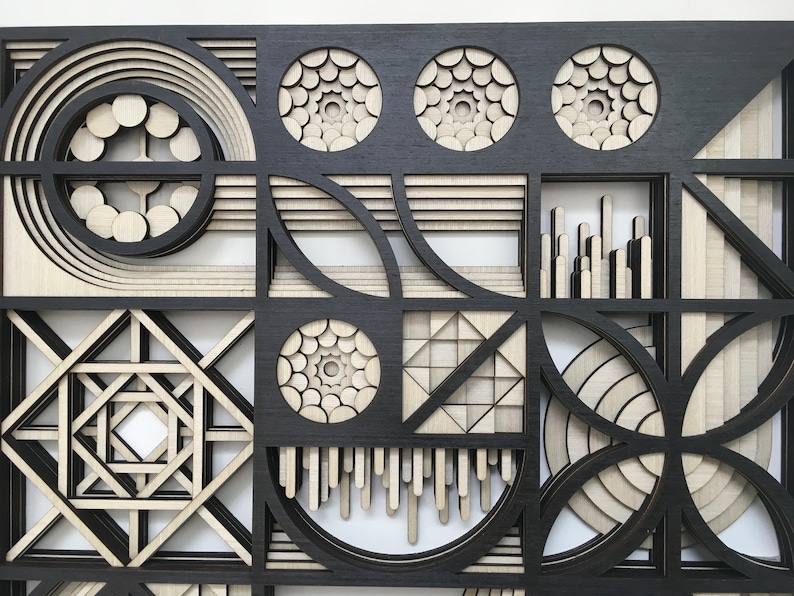 May include: A black and white geometric wall art piece with a layered design. The piece is made of wood and features a variety of shapes, including circles, squares, and triangles.