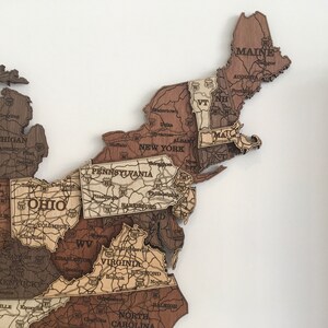 May include: A wooden map of the United States with each state outlined and labelled. The map is made of different shades of brown wood and features major cities and highways.