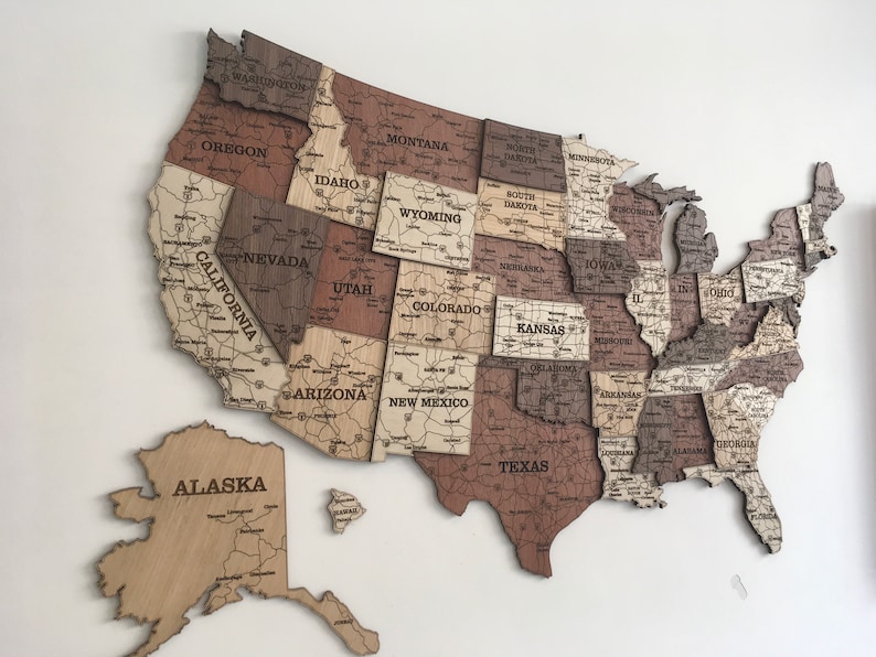 May include: A wooden map of the United States with each state outlined and labelled. The map is made of different shades of brown wood and has a light brown background.