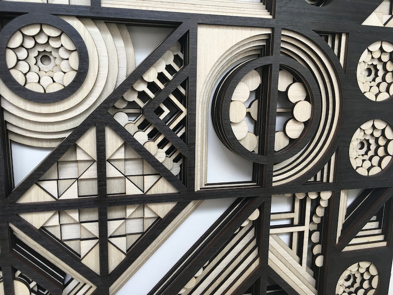 May include: Abstract geometric wall art made of layered wood with a black and white color scheme. The design features circles, squares, and triangles.