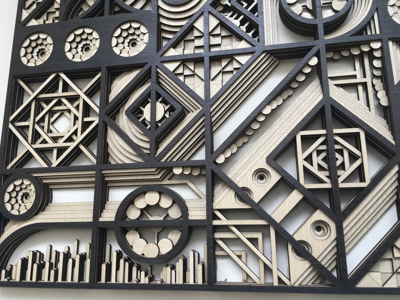 May include: A black and white geometric wall art piece made of wood. The piece is made up of various shapes and patterns, including circles, squares, and triangles. The piece is layered and has a 3D effect.