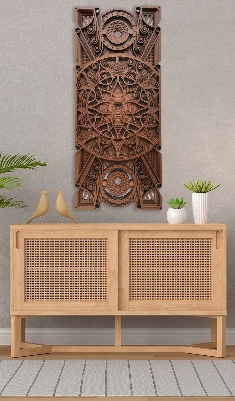 Puede incluir: Una pieza de arte de pared de madera con un dise&ntilde;o geom&eacute;trico en tonos marrones. El arte est&aacute; colgado en una pared gris claro sobre un gabinete de madera con un frente de rat&aacute;n tejido.