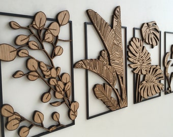 May include: Wooden wall art featuring botanical designs. The set includes four framed pieces with laser-cut leaves and branches in natural wood tones. Each piece is set within a black metal frame, creating a modern, nature-inspired aesthetic.