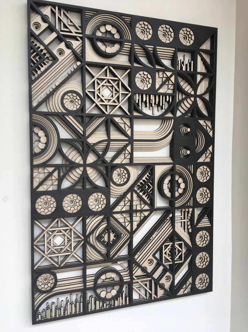 May include: A black and beige geometric wall art piece made of layered wood. The design features circles, squares, and triangles.