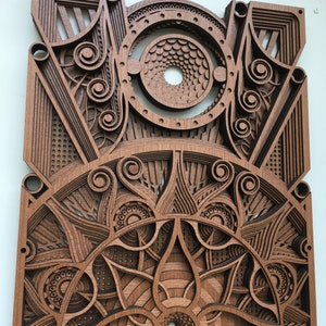 Puede incluir: Una pieza de arte de pared de madera con intrincados dise&ntilde;os cortados con l&aacute;ser. La pieza presenta un patr&oacute;n circular con un agujero central y m&uacute;ltiples capas de formas geom&eacute;tricas.