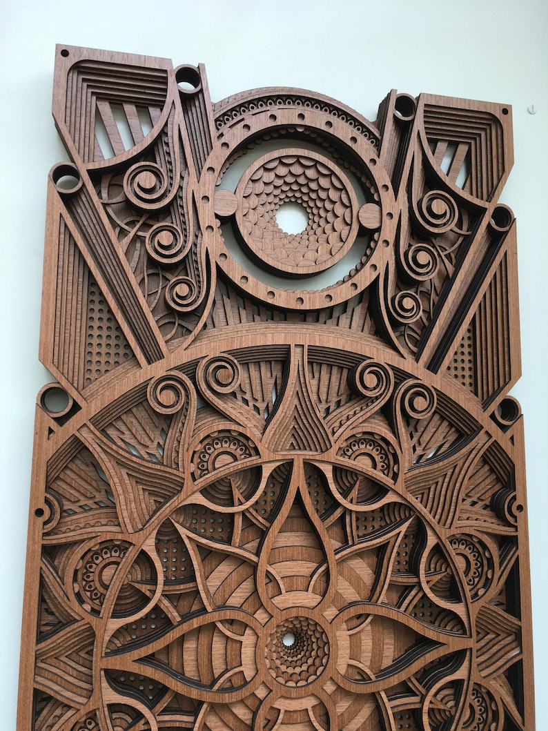 Puede incluir: Una pieza de arte de pared de madera con intrincados dise&ntilde;os cortados con l&aacute;ser. La pieza presenta un patr&oacute;n circular con un agujero central y m&uacute;ltiples capas de formas geom&eacute;tricas.