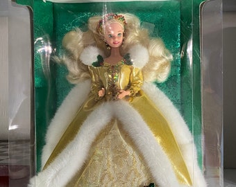 May include: A Barbie doll wearing a gold and white dress with a fur trim. The doll is in a clear plastic box with a green background and the words "Happy Holidays" and "Special Edition" on the box. The doll is wearing a crown and a necklace with a red jewel.