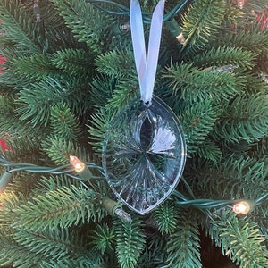 May include: A clear glass Christmas ornament with a white ribbon hanging on a green Christmas tree with white lights.