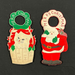 May include: Two vintage Christmas door hangers. One features a white cat in a basket with a green wreath and the words "Merry Christmas". The other features Santa Claus with a red bag and the words "Merry Christmas".