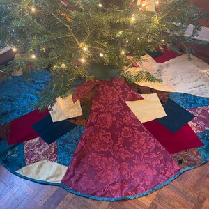 May include: A multi-colored patchwork Christmas tree skirt with a burgundy floral pattern in the center. The skirt is made of different fabrics, including velvet, satin, and brocade.