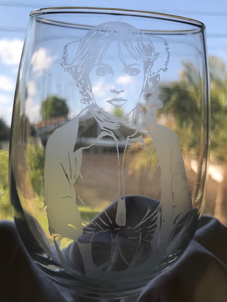 May include: A clear glass wine glass with a white etched design of a woman with a hairstyle similar to Princess Leia from Star Wars.