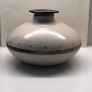 Puede incluir: Un jarrón de cerámica blanco con un borde marrón y una banda marrón alrededor del medio. El jarrón tiene un diseño moteado.
