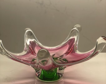 May include: A pink and green glass bowl with a unique, organic shape. The bowl has a wide, flat base and a raised center. The glass is clear and has a slight iridescent quality.