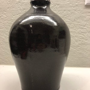 May include: A black ceramic vase with a rounded body and a flared neck. The vase has a glossy finish.