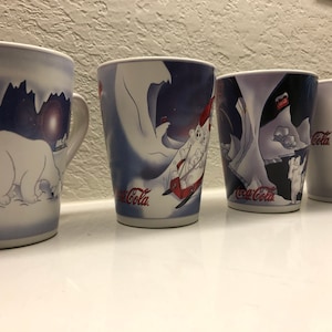 Puede incluir: Conjunto de cuatro tazas de cerámica blanca con escenas de invierno azules y blancas con osos polares y el logotipo de Coca-Cola.